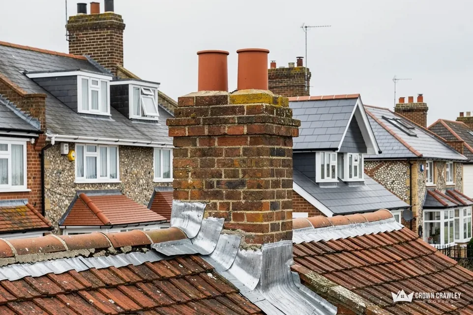 Chimney stack with orange pots and lead flashing among tiled roofs