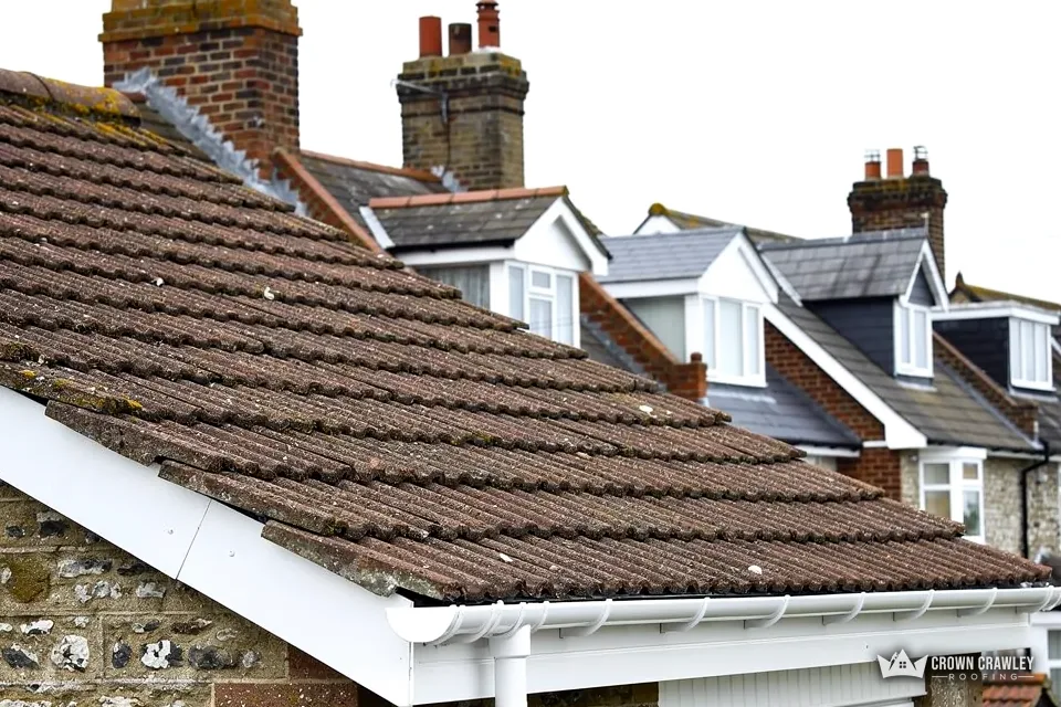 Moss-stained tiles above white fascias on a flint-walled house