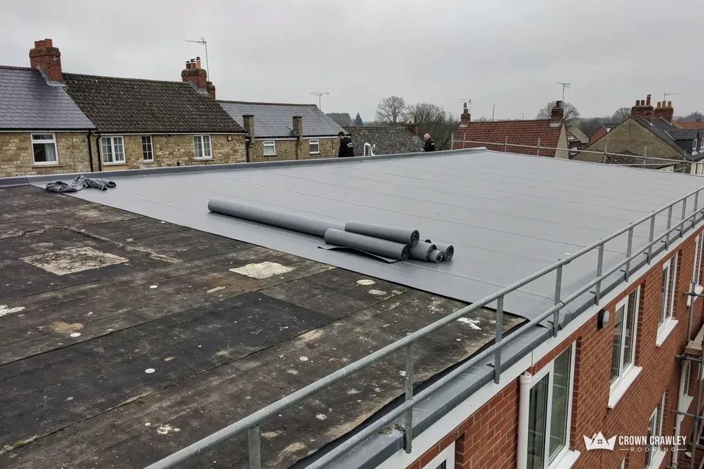 Grey single-ply flat roof with edge protection above a row of terraced houses