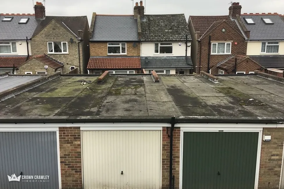 Mossy flat-roofed brick garage block with three up-and-over doors