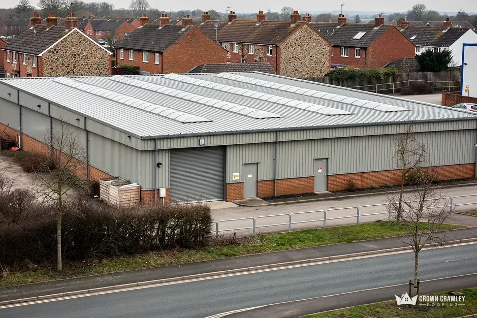 Large grey metal-clad industrial unit with long rooflights beside a road