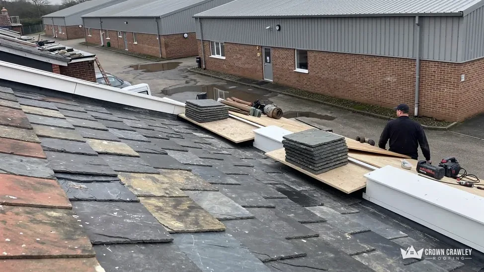 Roofer laying slate-effect sheets beside a large warehouse unit