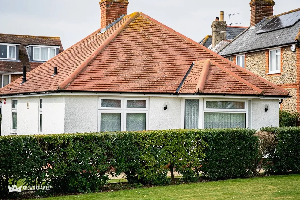 Red tiled hipped bungalow roof behind a neat hedge