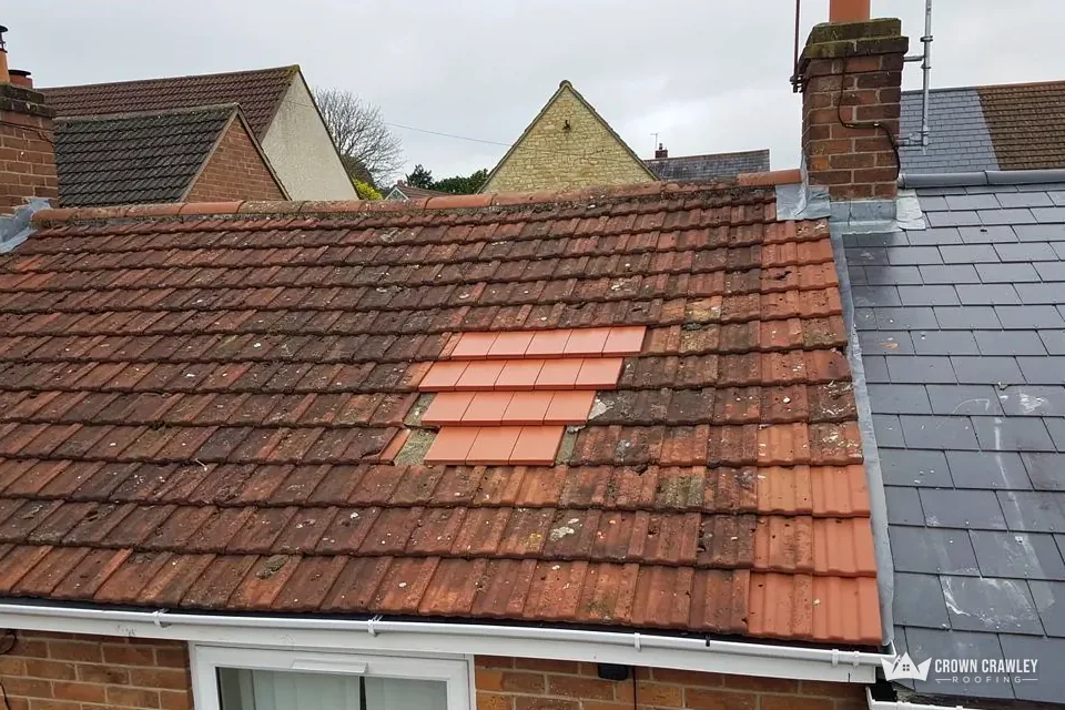 Roof slope with a patch of replacement tiles beside a slate roof