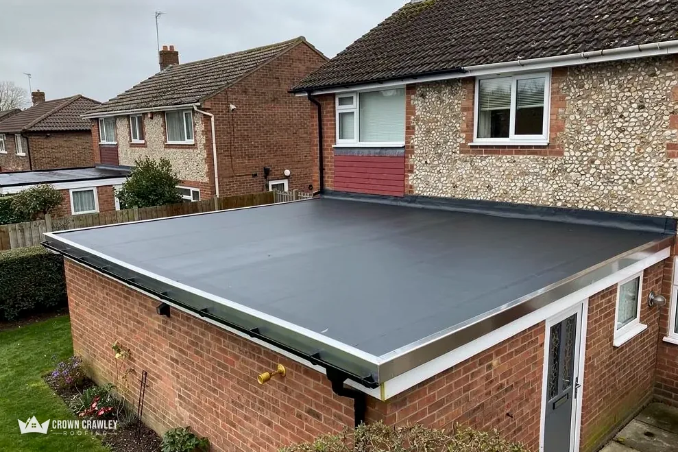 New grey EPDM flat roof on a brick extension beside a flint-walled house