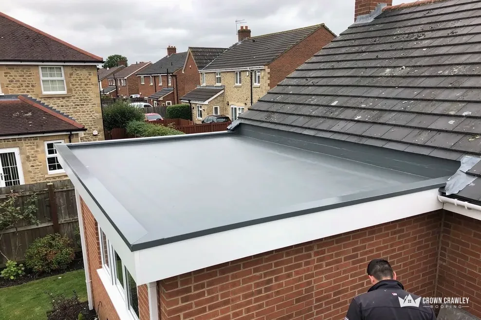 Newly laid grey flat roof on a brick extension with a roofer at work