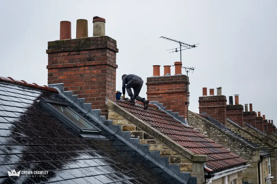 Roofer working near chimney stacks on a wet slate roof