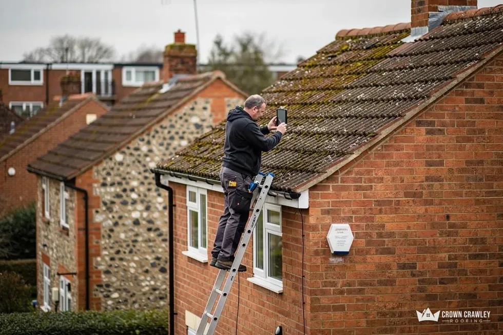 Roofer on a ladder inspecting moss on a tiled roof