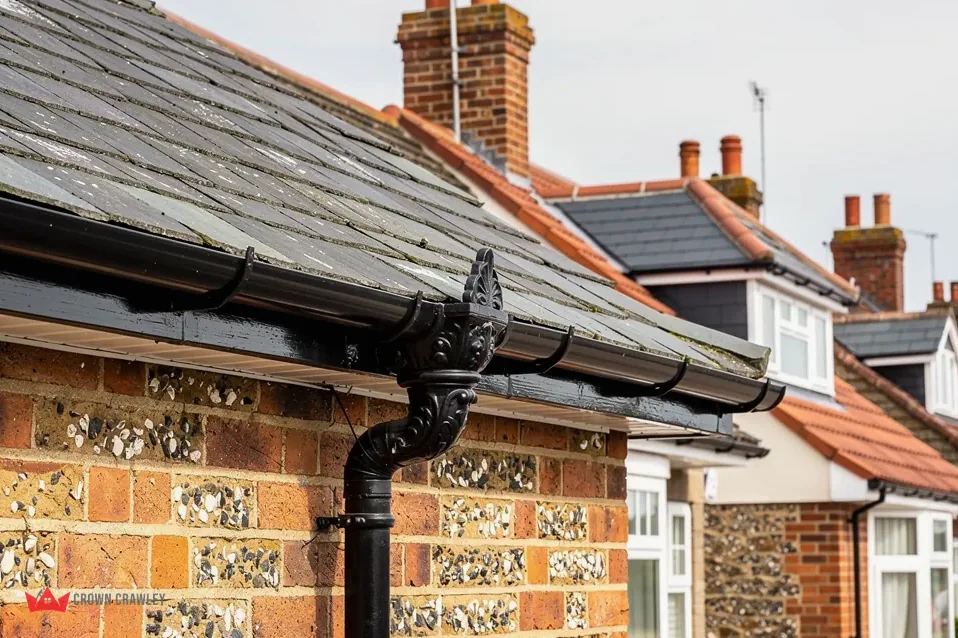 Black cast-style gutter and downpipe on a flint and brick wall