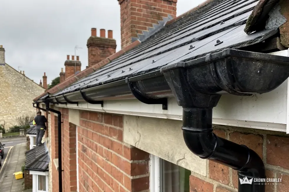 Black half-round guttering and downpipe on a brick house with a white soffit