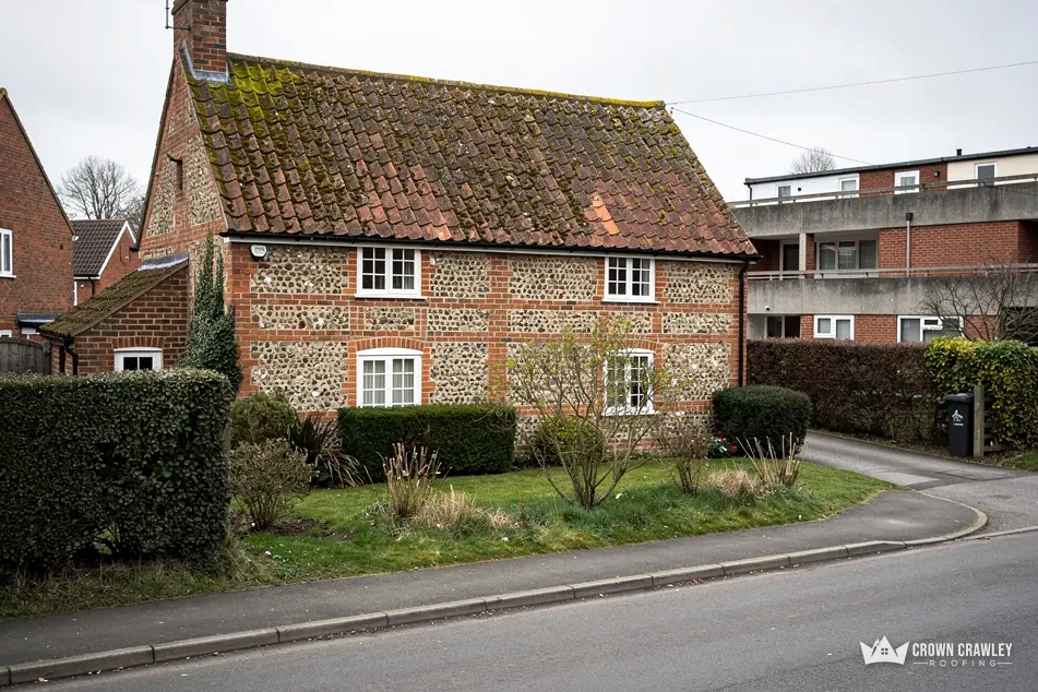 Flint-walled cottage with a clay tile roof on a village lane