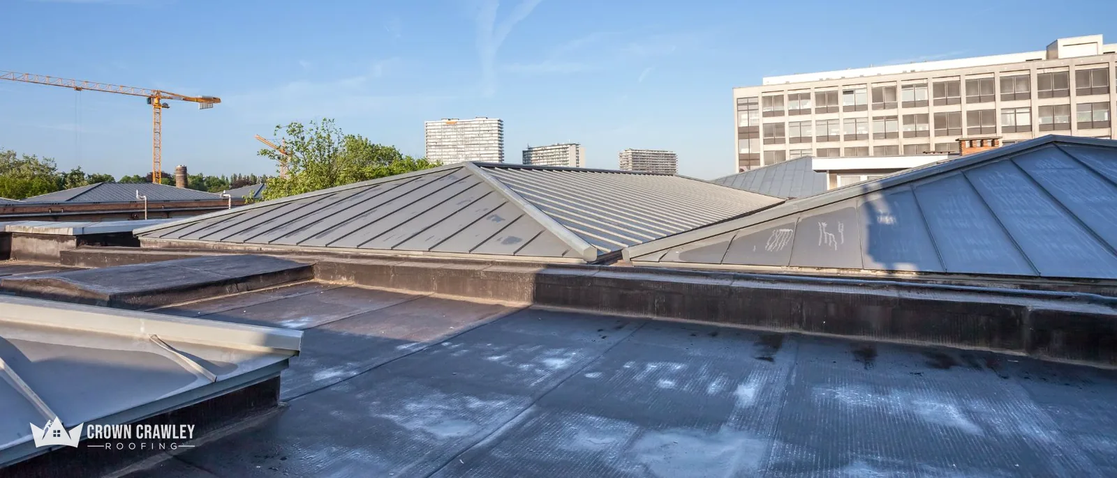 Flat roof with metal-clad rooflights beside a city skyline