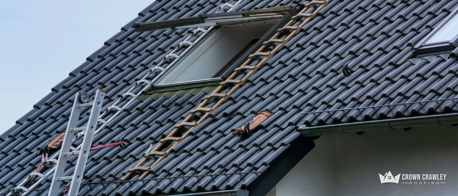 Black roof tiles with a roof window and ladder against a house