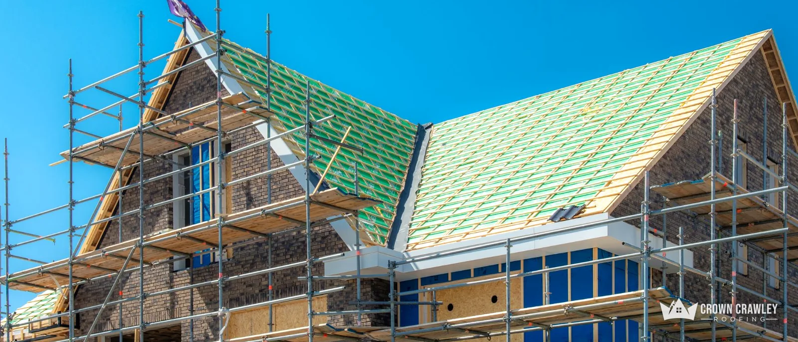 Brick house with scaffold and green roofing membrane across the slopes