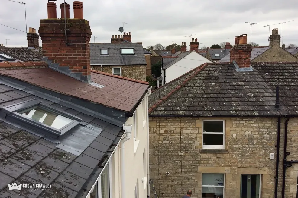 Slate and tiled roofs with a roof window beside a stone cottage