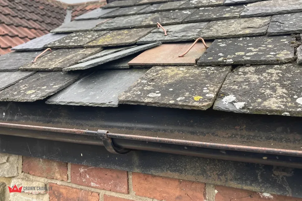 Old slates, damaged and slipped, above a cast-iron gutter
