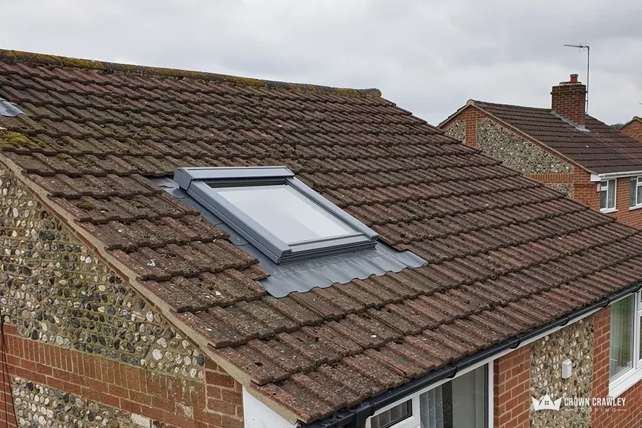 Roof window set into a brown tiled roof above a flint wall